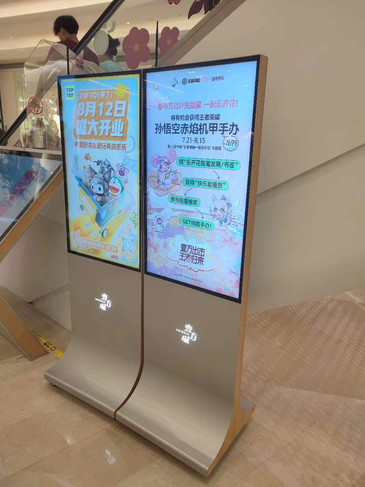 Two portrait digital displays installed beside a shopping mall escalator